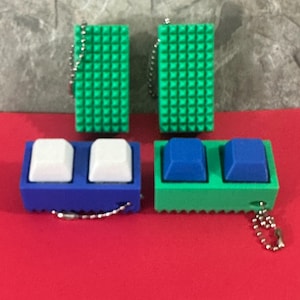 May include: Four keychains with a keyboard key theme. Two green rectangular keychains with a textured surface and two keychains with two keys each. One blue keychain with white keys and one green keychain with blue keys. All have a silver chain.