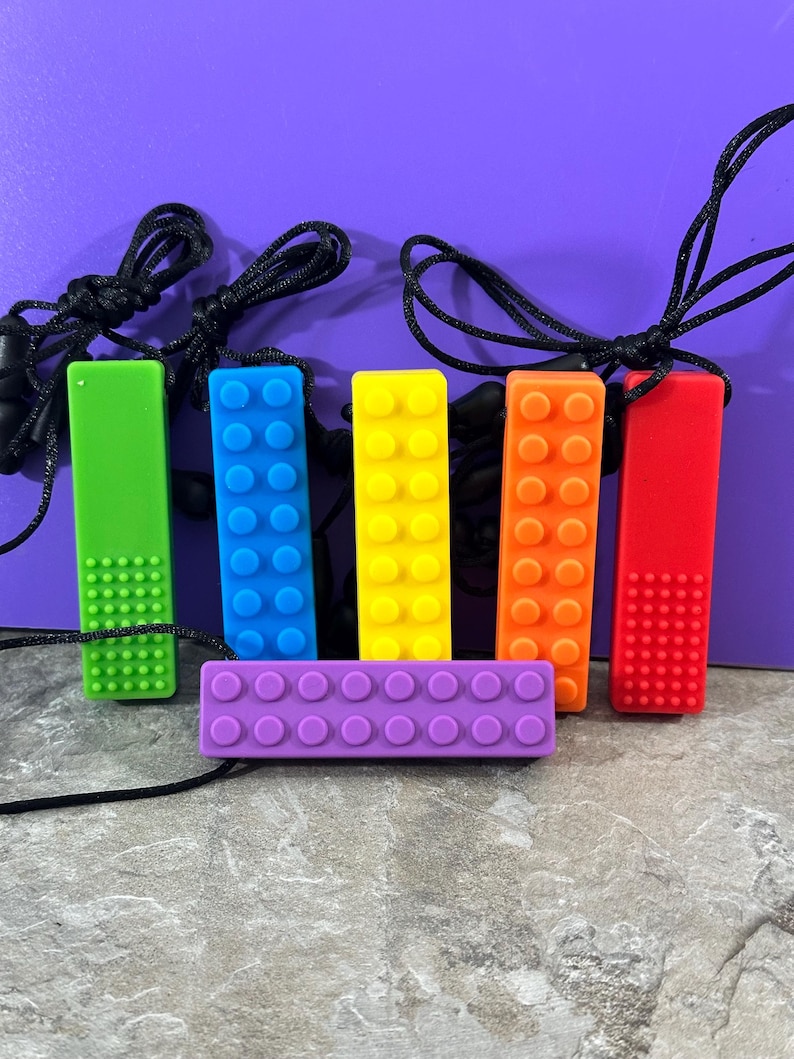 adult chewelry chew necklace - looks like a building brick block on the front and soothing bumps on the back. has a safety break away necklace. colors are: Red, orange. yellow, blue. green, purple