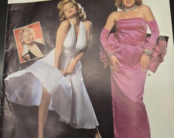 May include: Simplicity Costumes sewing pattern number 0668 for sizes 10, 12, and 14. The pattern features two different dress designs. The first dress is a white halter dress with a flowing skirt. The second dress is a pink strapless gown with a fitted bodice and a full skirt. The pattern includes the text "MARILYNTM and NORMA JEANETM are trademarks of the Estate of Marilyn Monroe. Licensed by CMG Worldwide Inc., Indpls, IN 46256 U.S.A. www.cmgww.com"