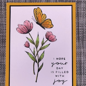 May include: A white card with a yellow border features a hand-drawn illustration of a butterfly and flowers. The text "I hope your day is filled with joy" is written in black ink.
