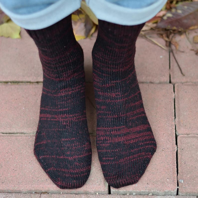 K&ouml;nnte beinhalten: Ein Paar schwarze und burgunderfarbene gestreifte Socken. Die Socken sind aus weichem, gestricktem Stoff.
