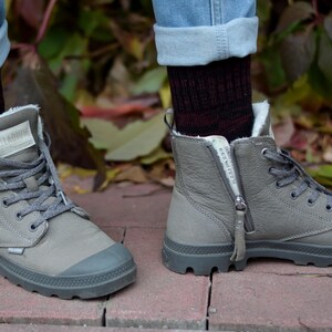 K&ouml;nnte beinhalten: Ein Paar graue High-Top-Stiefel mit einem Rei&szlig;verschluss an der Seite. Die Stiefel haben eine dicke Sohle und sind aus einem weichen, Wildleder-&auml;hnlichen Material gefertigt. Die Stiefel werden mit Jeans und Socken getragen.