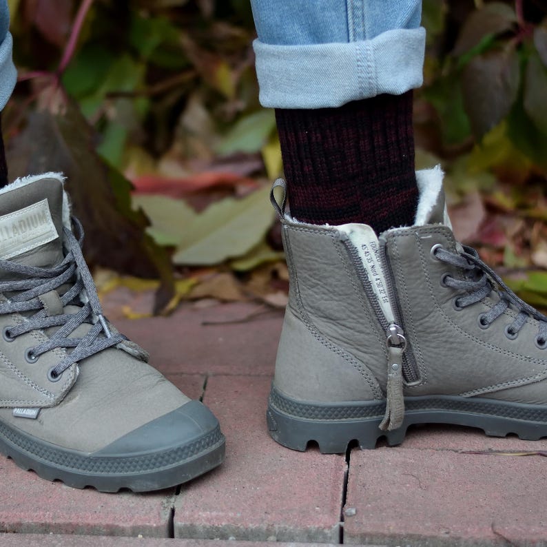 K&ouml;nnte beinhalten: Ein Paar graue High-Top-Stiefel mit einem Rei&szlig;verschluss an der Seite. Die Stiefel haben eine dicke Sohle und sind aus einem weichen, Wildleder-&auml;hnlichen Material gefertigt. Die Stiefel werden mit Jeans und Socken getragen.