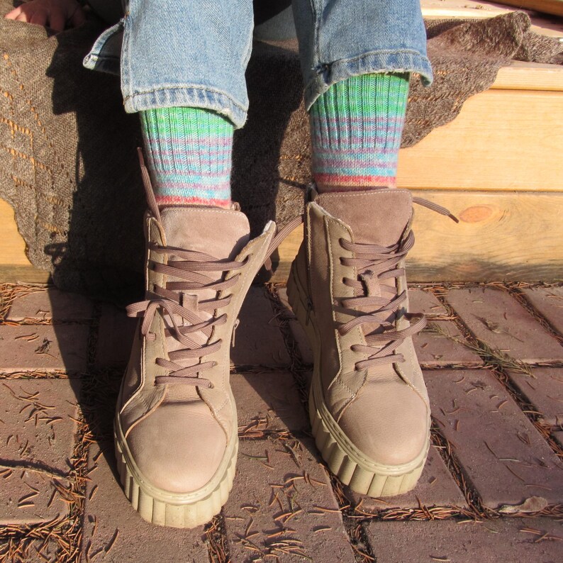 May include: A pair of light brown suede boots with thick soles and matching laces. The boots are worn with blue jeans and striped socks in shades of green, blue, and red.