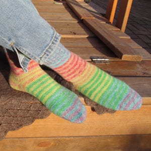 May include: A pair of colorful striped socks in shades of red, yellow, green, blue, and purple. The socks are worn with blue jeans. The socks are made of a soft, knitted material.