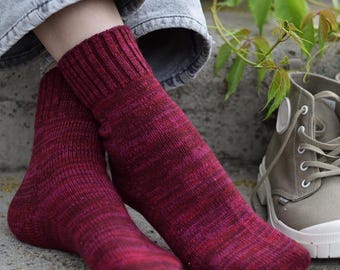 Könnte beinhalten: Handgestrickte Socken in Burgunder- und Rosatönen. Die Socken haben einen gerippten Bund und ein strukturiertes Design. Ein Paar graue Leinenschuhe ist im Hintergrund zu sehen.