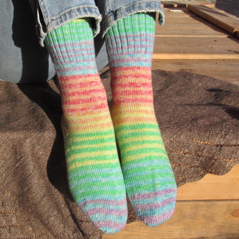 May include: A pair of colorful socks with a rainbow pattern. The socks feature bands of green, yellow, red, and blue. The socks are worn with blue jeans. The socks are made of a soft, knitted material.