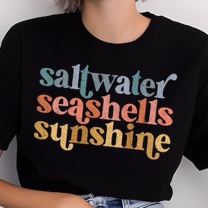 May include: Black t-shirt with a vintage-style graphic that reads "saltwater seashells sunshine" in rainbow colors.