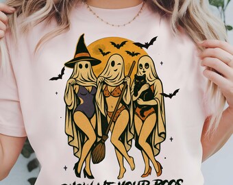 May include: A light pink t-shirt featuring a Halloween-themed graphic. The graphic depicts three ghost figures in lingerie, a witch hat, a broom, and a black cat, set against a full moon and bats. The text "SHOW ME YOUR BOOS" is at the bottom.