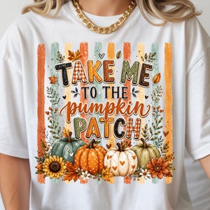 Może przedstawiać: Biały t-shirt z nadrukiem graficznym w pionowe paski w odcieniach pomarańczu, zieleni i kremu. Napis "TAKE ME TO THE PUMPKIN PATCH" wykonano różnymi czcionkami, w otoczeniu ilustracji dyń, słoneczników oraz jesiennych liści.