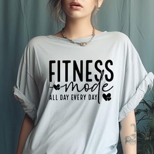 May include: Light blue t-shirt with black text that reads "Fitness mode all day every day" with two small hearts on either side of the word "mode".