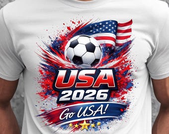 Könnte beinhalten: Weißes T-Shirt mit einem Fußball, der amerikanischen Flagge und dem Text "USA 2026 Go USA!" in Rot, Weiß und Blau. Das Design beinhaltet Sterne und einen Spritzeffekt.