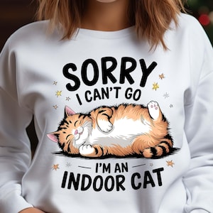 以下が含まれることがあります： 白いスウェットシャツに、寝ているオレンジと白の猫のグラフィックがプリントされています。テキストには「ごめんなさい、行けません。私は家猫です」と書いてあります。
