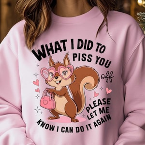 May include: Pink sweatshirt with a cartoon squirrel wearing heart-shaped sunglasses and holding a purse. The text on the sweatshirt reads "What I did to piss you off, please let me know I can do it again."
