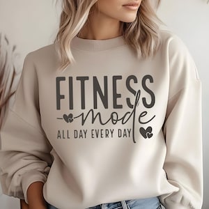 May include: A beige sweatshirt with the text "Fitness mode all day every day" in black lettering and two small hearts on either side of the word "mode".