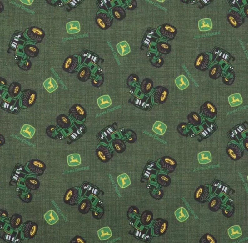 May include: A dark green fabric featuring a repeating pattern of small green tractors and yellow deer logos. The tractors are depicted in various orientations across the textile, interspersed with the iconic yellow deer emblem on a green square background.