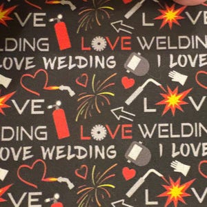 May include: Black fabric featuring a repeating pattern of white text reading LOVE WELDING and I LOVE, interspersed with red fire extinguishers, red hearts, yellow and orange sparks, grey welding helmets, white gloves, and circular saw blades.