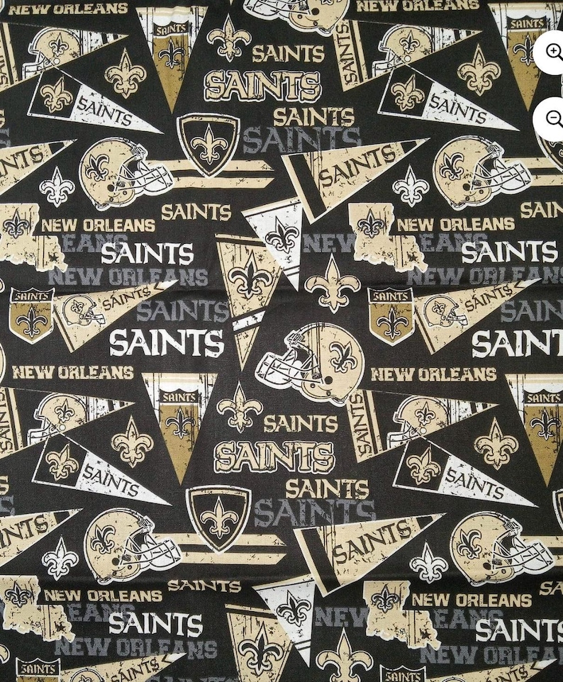 May include: A black fabric featuring a repeating pattern of New Orleans Saints football team graphics. The design includes gold and white football helmets, pennants with the text SAINTS, fleur-de-lis symbols, and the text NEW ORLEANS.