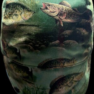 May include: A baseball cap featuring an all-over print of various fish swimming in a green underwater environment with rocks and aquatic plants. The design displays multiple fish species in shades of brown, green, and yellow against a green background.