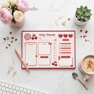 May include: A Daily Planner with a pink and white gingham design, featuring sections for to-do lists, notes, goals, and reminders. The planner includes cherry and heart illustrations. A rose gold pen and paper clips are also visible.