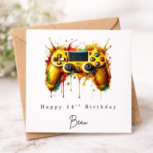 May include: A square greeting card featuring a watercolour-style illustration of a yellow and orange video game controller with paint splatters. The text reads Happy 14th Birthday and the name Beau in a black script font, set against a white background.