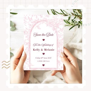 May include: A wedding invitation card with the text "Save the Date" in a decorative arch. The card is white with a pink floral design and the names "Kelly & Melanie". The date is Friday 18th June 2027.