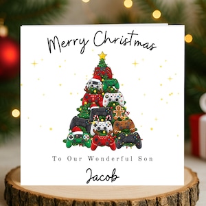 May include: A festive Christmas card with a white backdrop, showcasing a Christmas tree constructed from various colourful video game controllers. The card displays the text "Merry Christmas" and "To Our Wonderful Son Jacob". A gold star adorns the tree.