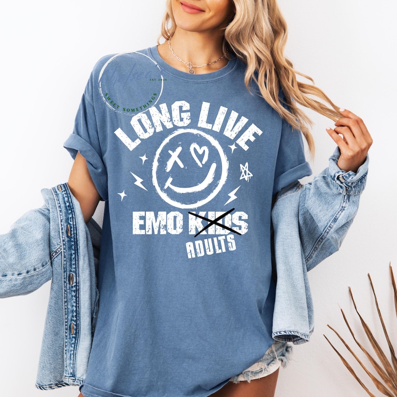 May include: A blue t-shirt with the text "LONG LIVE" above a smiley face with heart eyes and a crossed-out "EMO KIDS" with "ADULTS" below. The shirt has a relaxed fit.