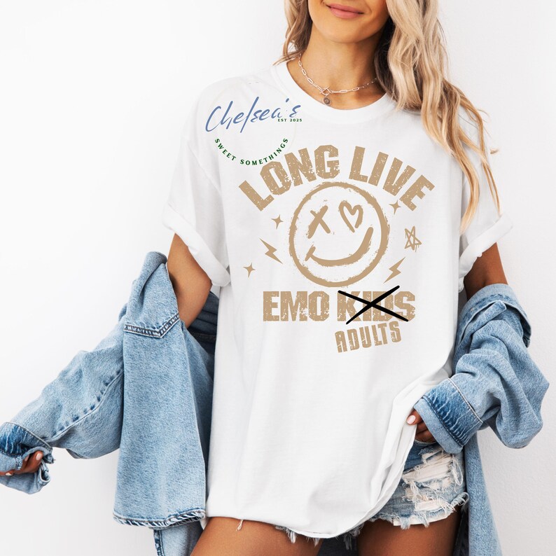 May include: White t-shirt with the text "LONG LIVE EMO KIDS" in a tan color. The design includes a smiley face with an X for eyes and a heart, plus lightning bolts and stars. The shirt is part of the "Chelsea's Sweet Somethings" collection.