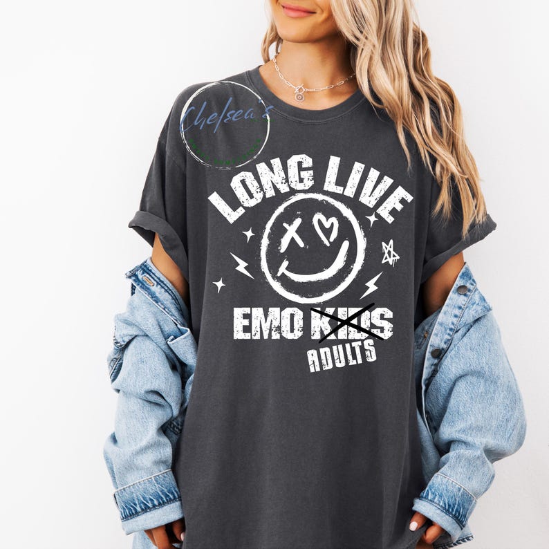 May include: Dark gray t-shirt with the text "LONG LIVE" above a smiley face with an X for eyes and a heart, plus the text "EMO KIDS" crossed out and replaced with "ADULTS". The shirt has rolled-up sleeves.