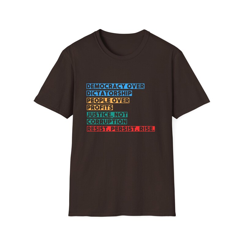 May include: A dark brown t-shirt with a white, blue, orange, and red graphic print that reads "Democracy Over Dictatorship, People Over Profits, Justice, Not Corruption, Resist. Persist. Rise."