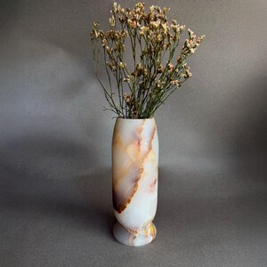 Pode incluir: Um vaso decorativo de pedra branca e &acirc;mbar, com flores secas. O vaso tem uma base arredondada e uma forma esguia e alongada. As veias naturais da pedra criam um padr&atilde;o &uacute;nico.