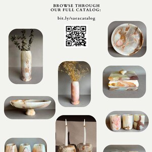 Pode incluir: An&uacute;ncio da Sa&eacute;a, com objetos de arte em pedra. A imagem mostra v&aacute;rios itens de pedra, incluindo vasos, tigelas, casti&ccedil;ais e um prato decorativo. O texto inclui o nome da marca, o site e um c&oacute;digo QR para navegar no cat&aacute;logo.