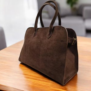 May include: A brown suede handbag with a top handle and a buckle closure.