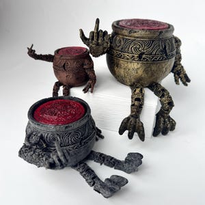 May include: Three detailed, hand-painted figurines of animated pots with arms and legs. The pots are in shades of brown, gold, and grey, with red, textured tops. One pot is giving the middle finger.