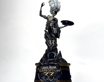 Puede incluir: Una figura detallada que muestra una silueta espectral con cabello blanco y un cuerpo oscuro y fragmentado, sosteniendo un disco negro. La base tiene la inscripción Clair Obscur Expedition 33 y el número 33 en letras doradas.