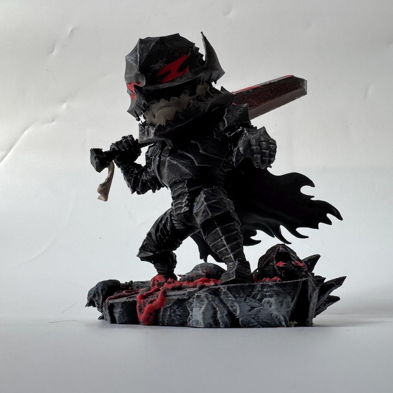 Puede incluir: Una figura negra de un guerrero con armadura, sosteniendo una gran espada roja. La figura tiene un casco con detalles rojos y una capa negra. La base es un terreno rocoso con detalles rojos.