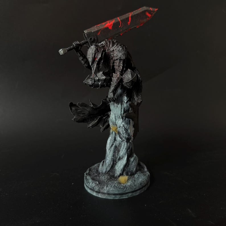 Puede incluir: Una figura detallada de un guerrero con armadura oscura sobre una base de piedra texturizada. La figura lleva una armadura negra dentada con detalles rojos y sostiene una espada masiva y desgastada sobre los hombros. La capa fluye detr&aacute;s.