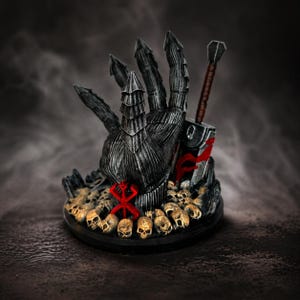 Puede incluir: Una escultura detallada, de color gris oscuro, de una mano con dedos en forma de garra, sosteniendo una espada. La base está adornada con calaveras y un emblema rojo. El diseño tiene un tema de fantasía.