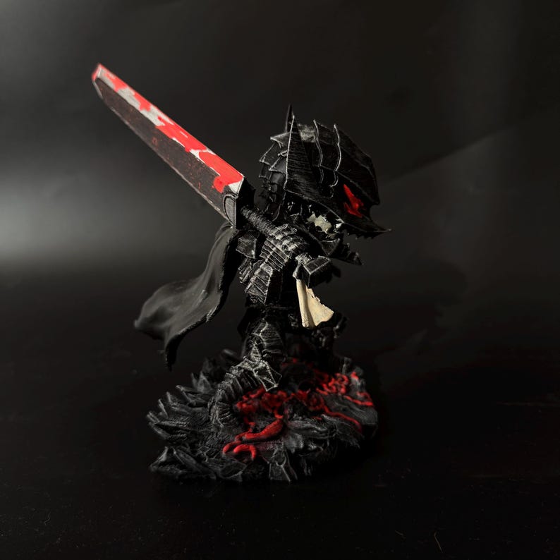 Puede incluir: Figura negra de un guerrero con armadura, sosteniendo una gran espada con una hoja roja. La figura tiene una capa y est&aacute; sobre una base texturizada con detalles rojos. El casco del guerrero tiene ojos rojos.