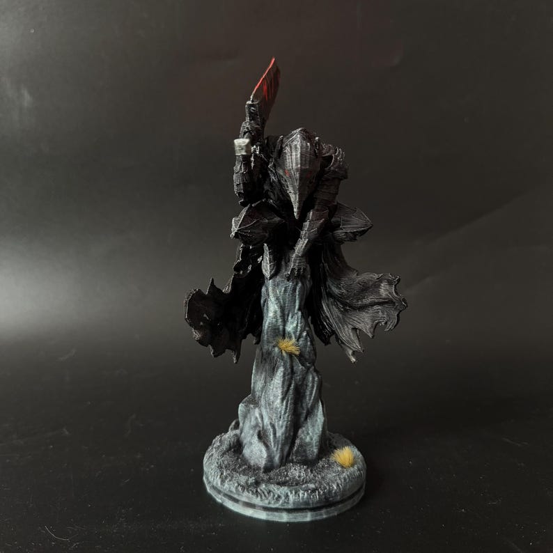 Puede incluir: Una figura oscura y texturizada de un caballero con armadura sobre una base rocosa. El caballero lleva un casco puntiagudo y una capa fluida, sosteniendo en alto un arma grande con hoja roja. La figura est&aacute; representada en negro y gris.