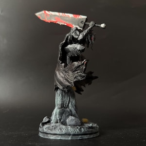 Puede incluir: Una figura pintada de un guerrero con armadura negra y capa ondeante, sobre una base gris texturizada. El personaje sostiene una espada grande y pesada sobre el hombro, con una hoja met&aacute;lica que presenta salpicaduras de pintura roja.