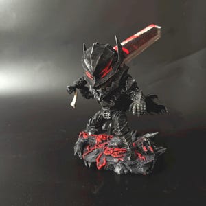 Puede incluir: Figura negra y roja de un personaje con armadura, sosteniendo una gran espada. La figura est&aacute; sobre una base rocosa con detalles rojos. La espada tiene una hoja roja y plateada. El personaje lleva un casco con detalles rojos.