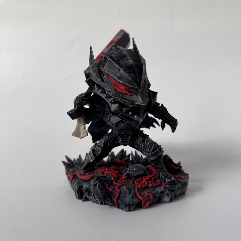 Puede incluir: Figura negra de un guerrero con armadura, con detalles rojos en el casco y la base. La figura sostiene una espada grande y un peque&ntilde;o objeto con forma de hueso. La base tiene una apariencia rocosa texturizada con vetas rojas.