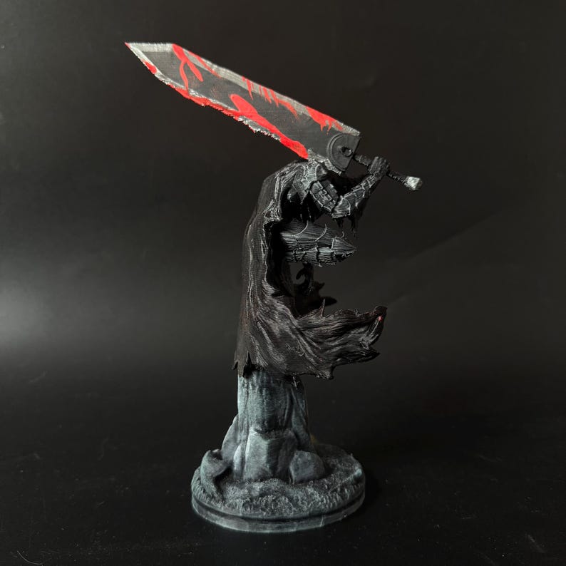 Puede incluir: Una figura en miniatura pintada de un guerrero con armadura oscura y una capa negra fluida, sobre una base rocosa. La figura sostiene una espada grande y pesada con una hoja negra que presenta marcas rojas dentadas sobre el hombro.