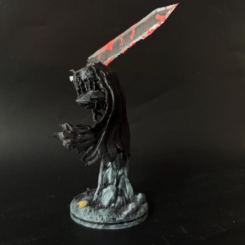 Puede incluir: Una figura en miniatura de un guerrero con una capa negra fluida y armadura, sosteniendo una gran espada transl&uacute;cida con detalles pintados en rojo. La figura se apoya sobre una base texturizada de color gris claro sobre fondo negro.