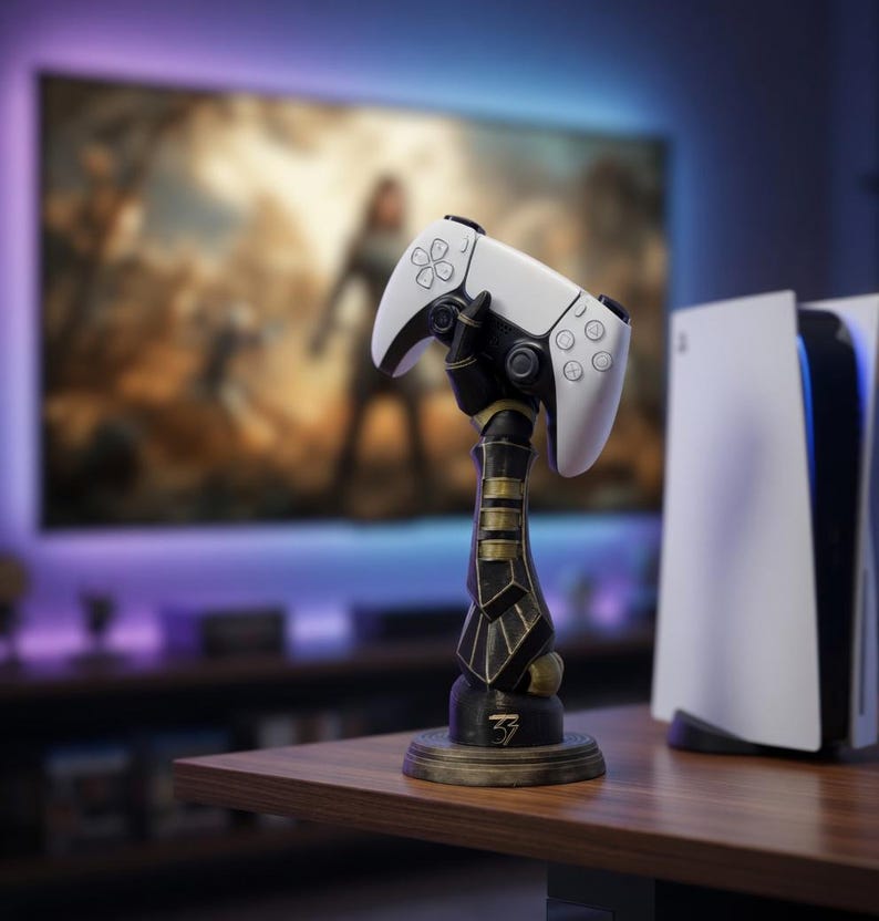 May include: A white and black wireless game controller held by a black and gold robotic hand stand. The stand features a circular base with the number 33 engraved on the front. The controller has standard buttons, joysticks, and a touchpad.