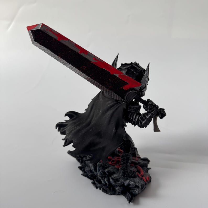 Puede incluir: Figura negra de un guerrero sosteniendo una gran espada con detalles rojos. El guerrero lleva una armadura y una capa, de pie sobre una base texturizada con detalles rojos. La espada tiene un dise&ntilde;o sangriento.