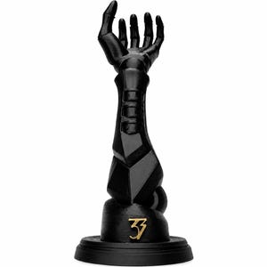 May include: A matte black sculptural object depicting a robotic arm extending upwards with an open hand. The forearm features segmented geometric plating. At the base, a circular stand displays the gold-coloured number 33 in a stylised font.