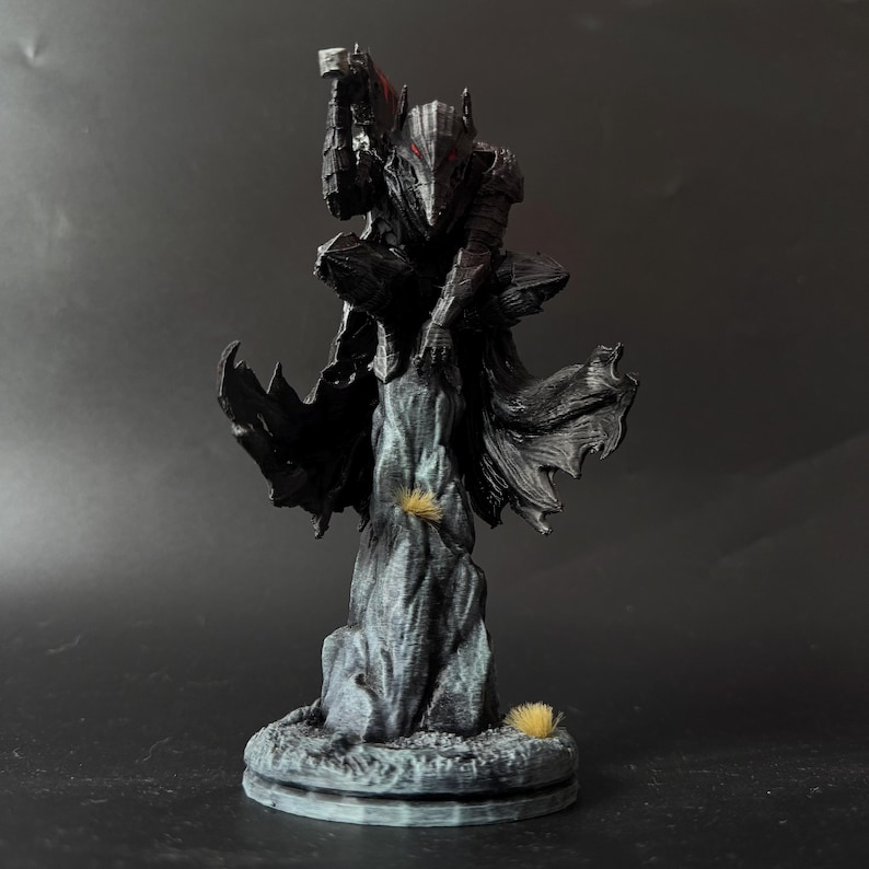 Puede incluir: Una figura impresa en 3D de color gris oscuro de un caballero con armadura completa, agachado sobre una formaci&oacute;n rocosa irregular. El caballero lleva un casco puntiagudo con detalles oculares rojos y una capa fluida, con una espada en alto.